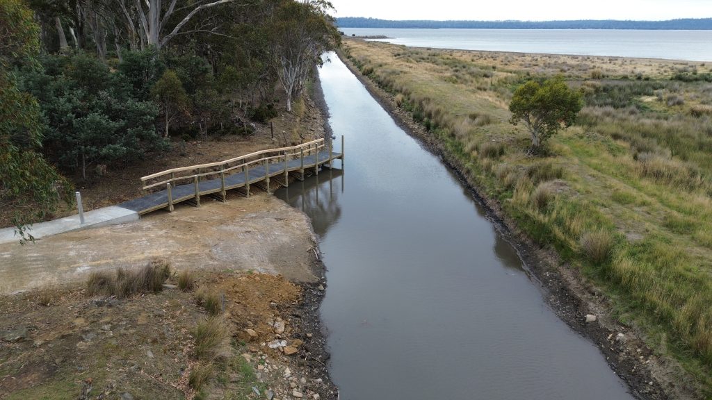 Image of a wooden walkway at Lake Crescent in Tasmania. The area is surrounded by bush with the lake in the background.